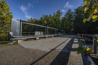 a paved walkway with a metal railing leading to a green bridge in a forest with trees and water