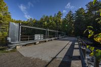 a paved walkway with a metal railing leading to a green bridge in a forest with trees and water