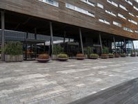 outside dining area with tables and chairs on large pavement walkway outside building with roof and wooden structure