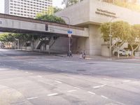 pedestrians crossing an intersection with pedestrian light above road entrance and building to right side with traffic lights in foreground