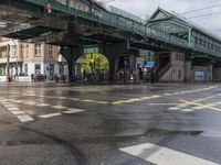 people are crossing the street under a green bridge, while rain falls on them in this photo