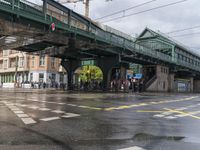 people are crossing the street under a green bridge, while rain falls on them in this photo