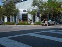 people crossing the street in front of an albla building on the corner of the road