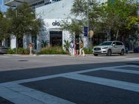 people crossing the street in front of an albla building on the corner of the road