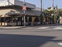 people are sitting outside of a cafe in the day time, on the corner and in front of the street