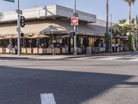 people are sitting outside of a cafe in the day time, on the corner and in front of the street