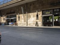 a line of people are waiting outside of a restaurant under a bridge near the city street