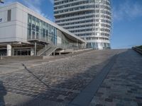 people walking up a brick walkway near tall white buildings in a city setting on a sunny day