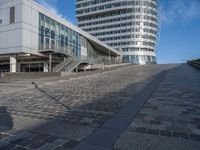 people walking up a brick walkway near tall white buildings in a city setting on a sunny day