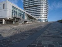 people walking up a brick walkway near tall white buildings in a city setting on a sunny day