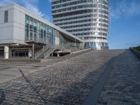 people walking up a brick walkway near tall white buildings in a city setting on a sunny day