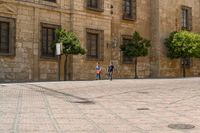 people walking up the sidewalk on a street near some buildings with trees in front of them