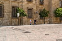 people walking up the sidewalk on a street near some buildings with trees in front of them