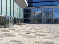 two people walking through an empty courtyard with many glass buildings in the background from the perspective of a parked motorcycle