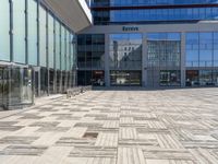 two people walking through an empty courtyard with many glass buildings in the background from the perspective of a parked motorcycle