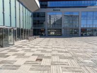 two people walking through an empty courtyard with many glass buildings in the background from the perspective of a parked motorcycle