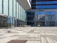 two people walking through an empty courtyard with many glass buildings in the background from the perspective of a parked motorcycle