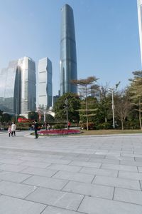 a group of people are walking around in the city on a sunny day with skyscrapers in the background