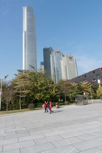 a group of people are walking around in the city on a sunny day with skyscrapers in the background