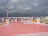 people walking and jogging across a large concrete plaza under cloudy skies with pink and yellow accents