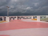 people walking and jogging across a large concrete plaza under cloudy skies with pink and yellow accents