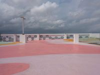 people walking and jogging across a large concrete plaza under cloudy skies with pink and yellow accents