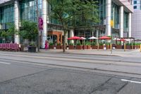 people walking on a sidewalk in front of a building next to trees and other outdoor furniture