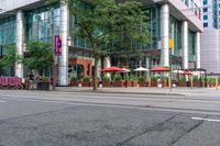 people walking on a sidewalk in front of a building next to trees and other outdoor furniture