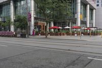 people walking on a sidewalk in front of a building next to trees and other outdoor furniture