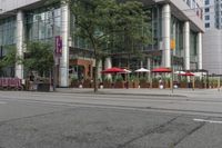 people walking on a sidewalk in front of a building next to trees and other outdoor furniture