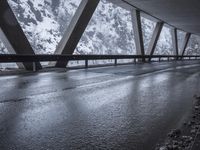 people walk under an overpass in the rain on a mountaintop road with snow