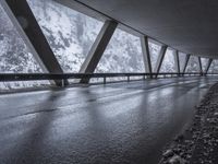 people walk under an overpass in the rain on a mountaintop road with snow