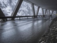 people walk under an overpass in the rain on a mountaintop road with snow