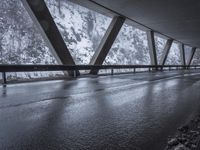 people walk under an overpass in the rain on a mountaintop road with snow