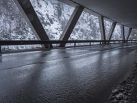 people walk under an overpass in the rain on a mountaintop road with snow