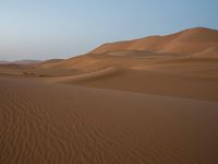 the person in the desert walks across a desert plain with large hills in the background