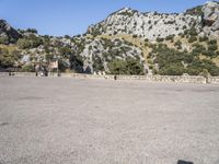 the shadow of a person in a parking lot, looking at a rock wall with a tree on top