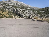 the shadow of a person in a parking lot, looking at a rock wall with a tree on top