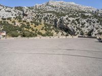 the shadow of a person in a parking lot, looking at a rock wall with a tree on top