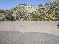 the shadow of a person in a parking lot, looking at a rock wall with a tree on top