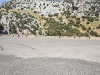 the shadow of a person in a parking lot, looking at a rock wall with a tree on top