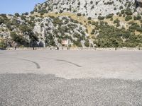 the shadow of a person in a parking lot, looking at a rock wall with a tree on top