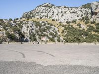 the shadow of a person in a parking lot, looking at a rock wall with a tree on top