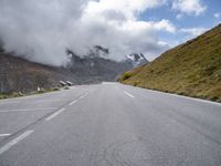 a person on an orange bike riding down a mountain road with the clouds coming over the mountains behind them