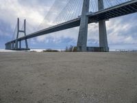 a person is riding their bike under a bridge on the beach in the background are buildings and water