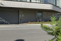 a person riding a skateboard near the road next to a building and bushes, with the back door closed