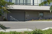 a person riding a skateboard near the road next to a building and bushes, with the back door closed