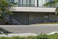 a person riding a skateboard near the road next to a building and bushes, with the back door closed