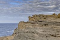 a person standing on the top of a cliff near the ocean and a dog that is laying on it