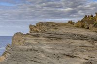 a person standing on the top of a cliff near the ocean and a dog that is laying on it